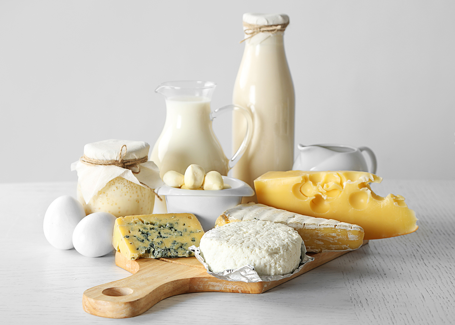 Angerichtete Käseplatte mit Milchflaschen, Eiern vor hellem Hintergrund