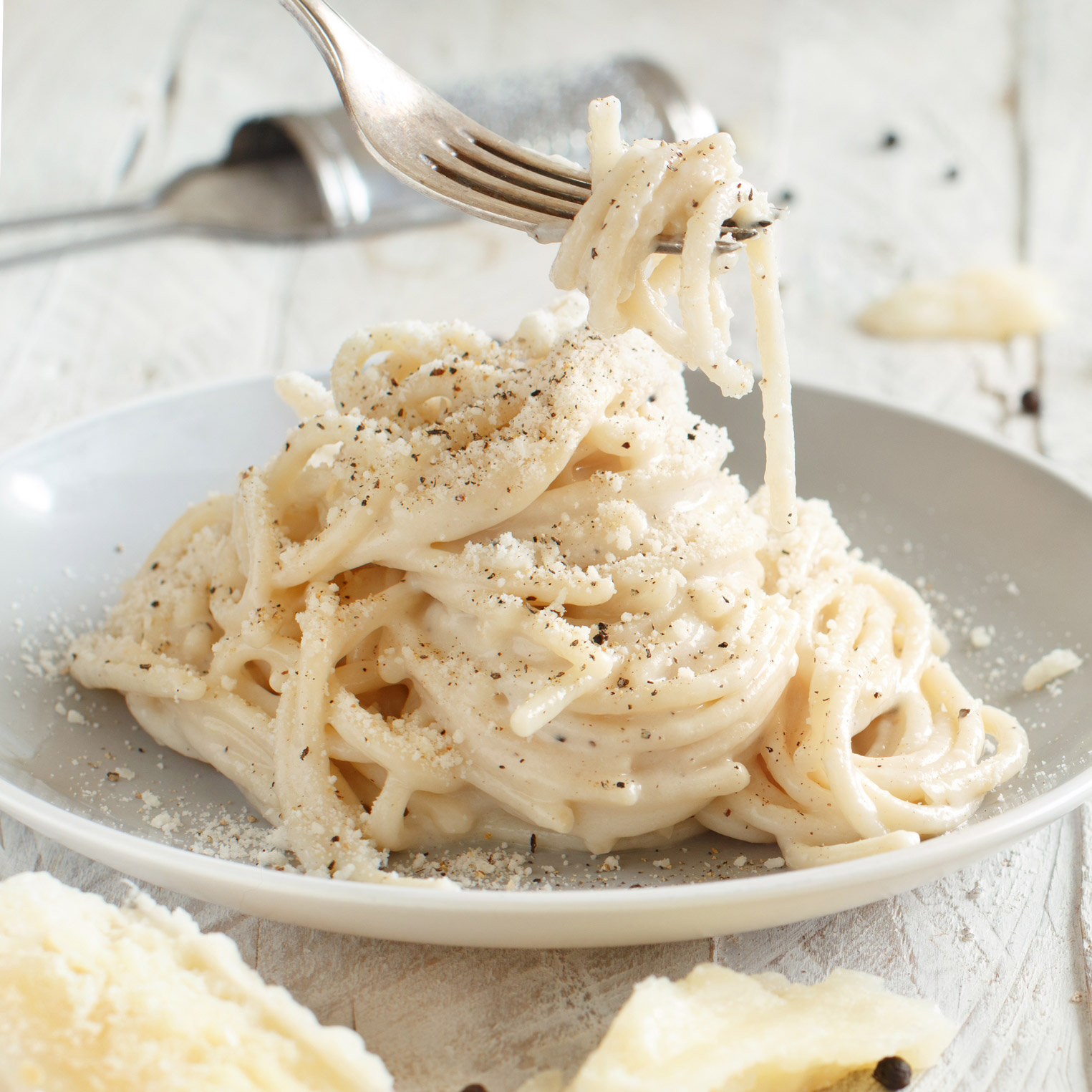 Nahaufnahme eines Tellers Pasta Cacio e Pepe, mit cremiger Pecorino-Sauce und frisch gemahlenem schwarzen Pfeffer, angerichtet auf einem weissen Teller mit Gabel.