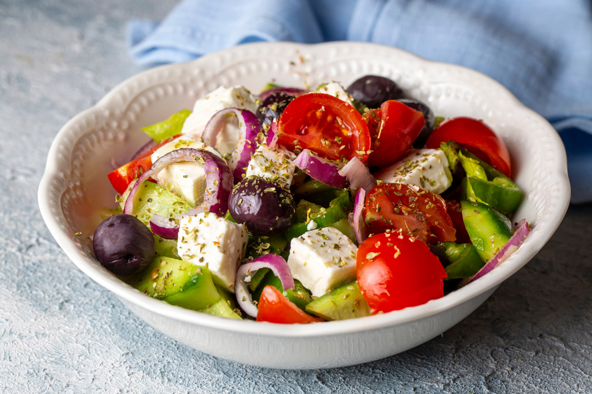 Traditioneller griechischer Bauernsalat (Horiatiki) mit frischen Tomaten, Gurken, roten Zwiebeln, Paprika, Feta und schwarzen Oliven in einer weissen Schüssel